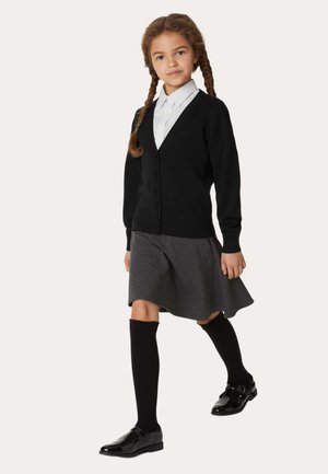 Schwarzer Cardigan mit V-Ausschnitt und Knopfleiste, getragen über einem weißen Hemd mit Kragen, grauem Rock, knielangen schwarzen Socken und glänzenden schwarzen Schuhen.