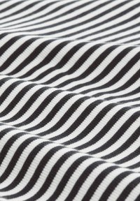 Tissu rayé noir et blanc avec une texture cannelée, comportant des rayures épaisses et fines alternées, disposées dans un motif ondulé.