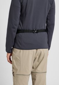 Jersey gris de manga larga con un acabado texturizado, que cuenta con un cinturón negro ajustable en la cintura. Combinado con pantalones beige claros.
