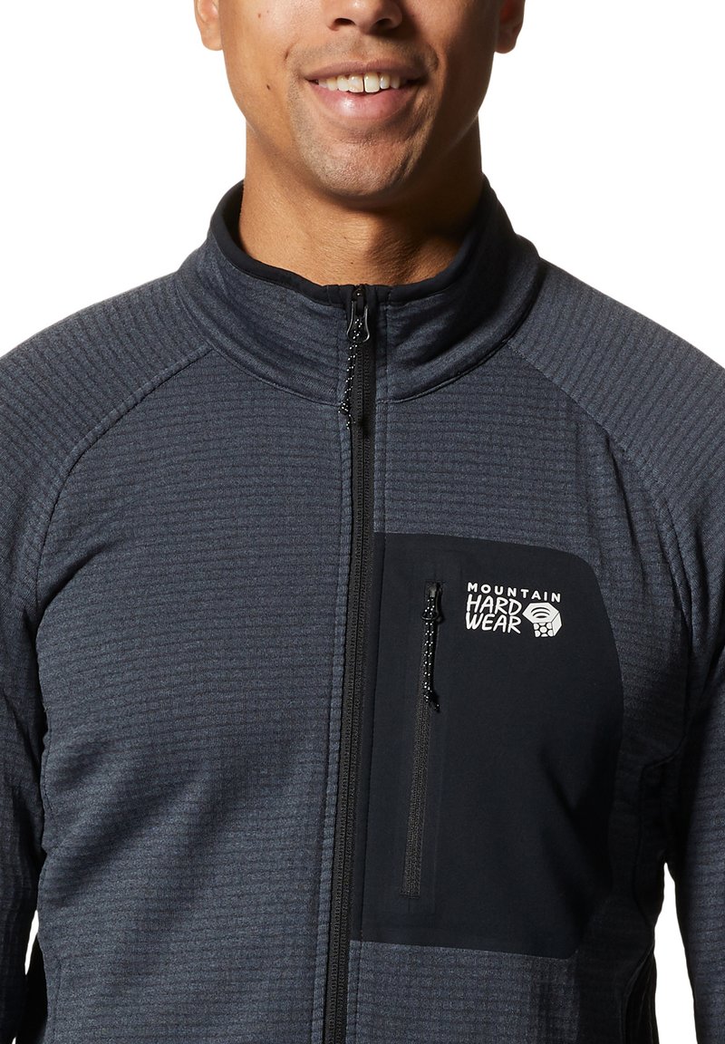 Kurtka polarowa w ciemnoszarym kolorze z teksturowanej tkaniny, z zapięciem na zamek, wysokim kołnierzem i czarną kieszenią na piersi z logo.