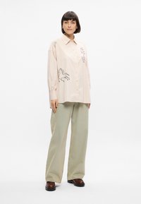 Ανοιχτό ροζ πουκάμισο με κεντημένο άλογο και λουλουδάτα σχέδια, σε συνδυασμό με φαρδιά παντελόνια σε φασκομηλιά και σκούρα καφέ παπούτσια.