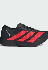 Sort atletisk sko med røde accenter, der har en tekstureret overdel, tre stribede designs og en LIGHTSTRIKE PRO sål til polstring.