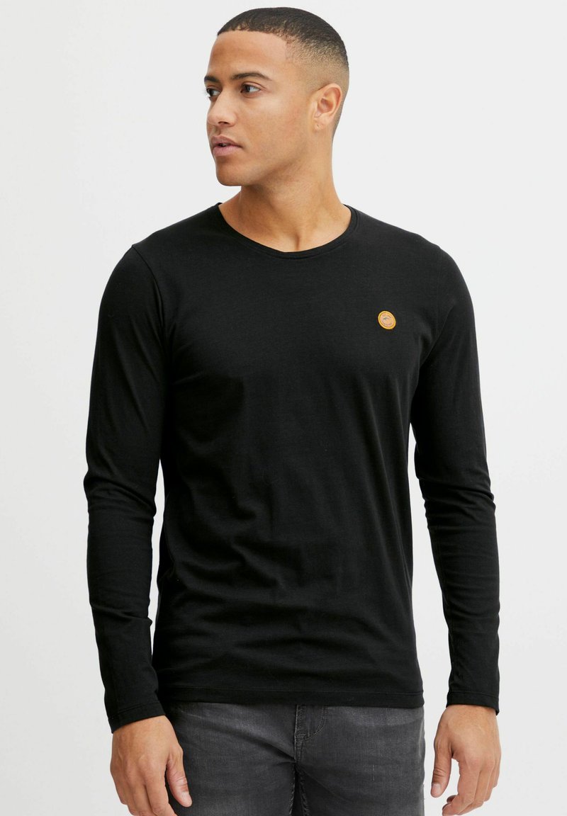 Black long-sleeve t-shirt made of cotton. Features a round neck and a small circular emblem on the chest. Smooth texture and fitted design.