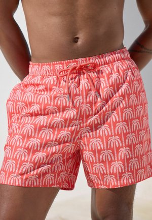 Coral swim shorts with a white palm tree pattern, featuring an elastic waistband and drawstring closure. Made from lightweight, smooth fabric.