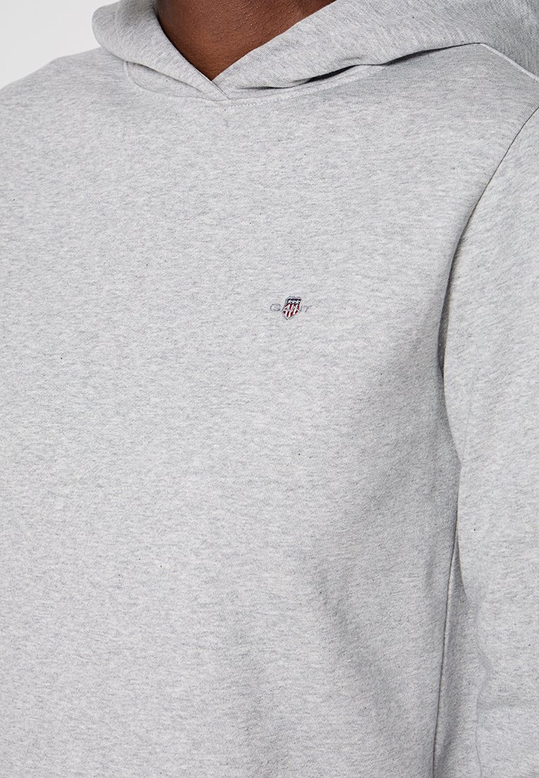 Sudadera gris claro hecha de un tejido suave, con un bolsillo frontal, capucha con cordones y un pequeño logotipo bordado en el pecho.