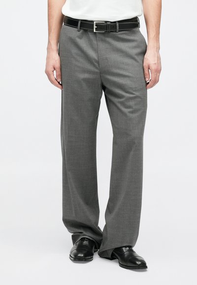 Γκρι παντελόνι με ίσια γραμμή, διακριτή υφή και μαύρη ζώνη με ασημένια αγκράφα. Φορεμένο με μαύρα παπούτσια.