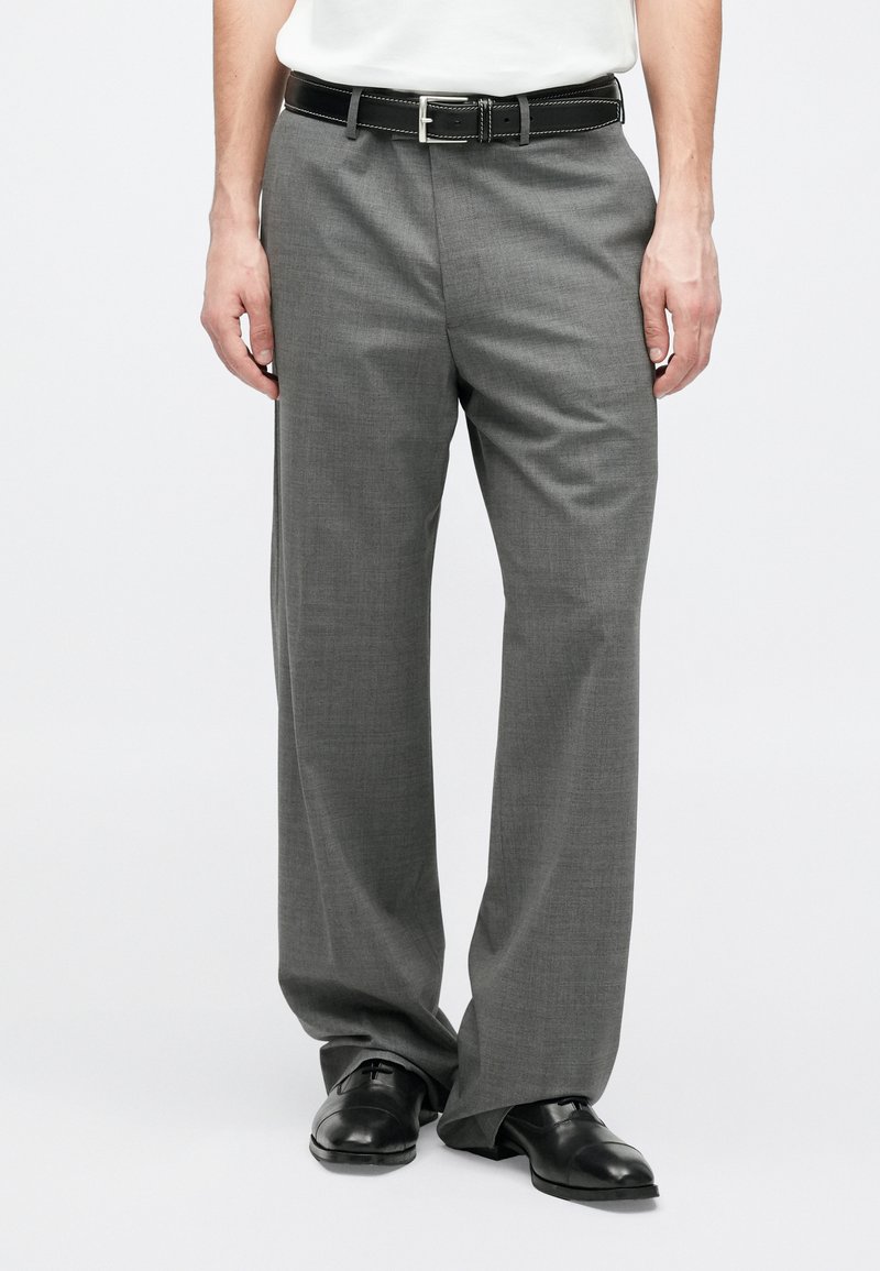 Graue Anzughose mit geradem Schnitt, feiner Textur und einem schwarzen Gürtel mit silberner Schnalle. Kombiniert mit schwarzen Anzugschuhen.