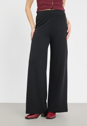 Wide-leg black pants made of soft fabric, featuring two front pockets and a comfortable waistband. Paired with red heeled boots.
