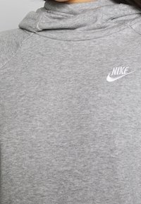 Grå huvtröja i bomullsblandning, med hög krage och en liten vit Nike-logga på bröstet. Slät textur och avslappnad passform.