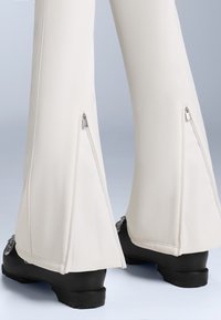 Fehér, oldalcipzáros, bővülő nadrág sima anyagból készült. Fekete, vastag talpú lábbeli, díszítő elemekkel a saroknál.