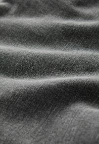 Hall hallikas kangas peene õmblustekstuuriga, millel on peened mõõtmelised lainetused ja sile, veidi läikiv pind.