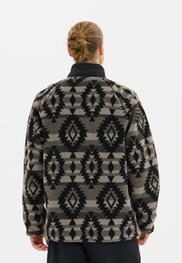 Fleece-Pullover mit hohem Kragen, der ein geometrisches Muster in Schwarz und Grau zeigt. Texturiertes Material mit lässiger Passform.