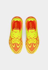Φωτεινά κίτρινα και πορτοκαλί παπούτσια τρεξίματος Reebok με κυματιστά μοτίβα, σε θέα από πάνω, σε λευκό απλό φόντο.