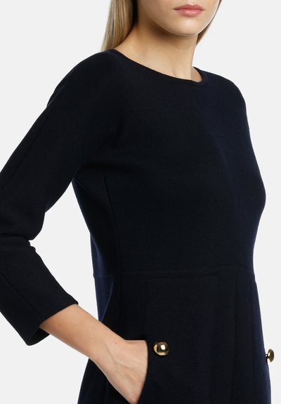 Navy-Strickkleid mit Rundhalsausschnitt, Dreiviertelärmeln und zwei vorderen Taschen, verziert mit goldfarbenen Knöpfen.