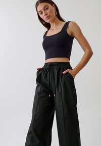 Crni skraćeni top s kvadratnim izrezom uparen s slobodnim, crnim kožnim hlačama koje imaju elastičnu waistband i bočne džepove.