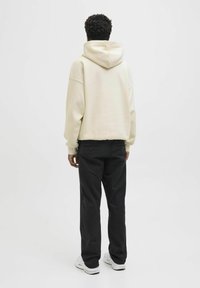 Crème-kleurige hoodie met een grote capuchon, ontspannen pasvorm, geribbelde manchetten, gecombineerd met zwarte broek en witte sneakers. Eenvoudig ontwerp, geen patronen.
