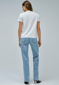 Camiseta blanca de algodón con cuello redondo, combinada con jeans rectos de color azul claro, que presentan bolsillos y una textura ligeramente descolorida.