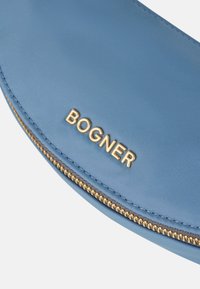 Borsa in nylon blu con hardware dorato. Caratterizzata da una chiusura con zip e dal nome del marchio "BOGNER" impresso in lettere dorate.