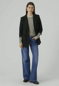 Svart blazer over en stripete langermet topp, kombinert med lyseblå merkelapper og svarte sko. Antrekket har en skreddersydd design.