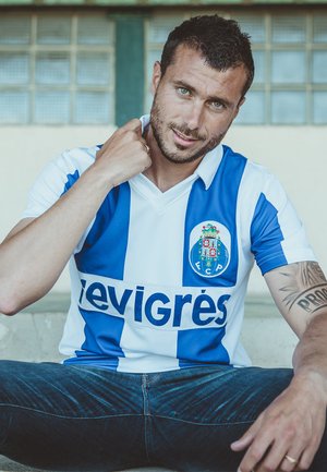 Wit en blauw gestreept voetbalshirt met logo "FC Porto" en tekst "evigrés." Gedragen met donkere jeans, zittend op een betonoppervlak.