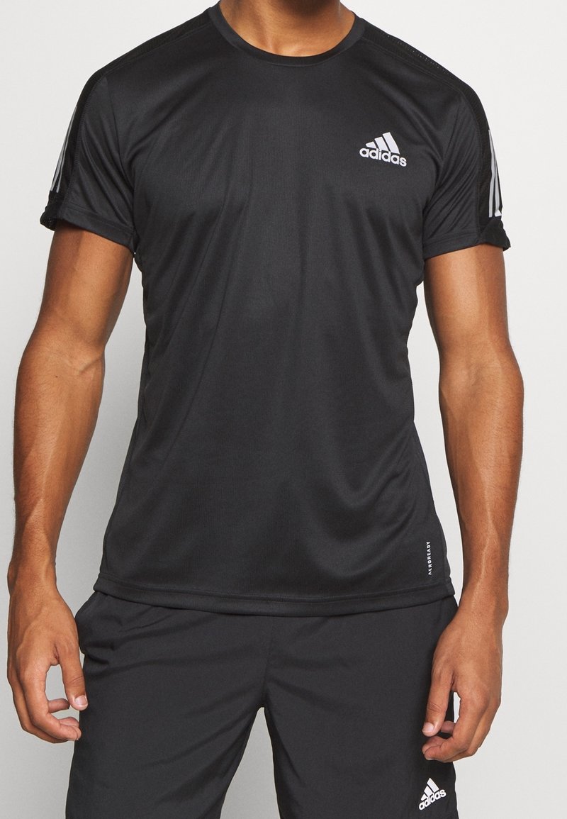 T-shirt de sport noir à manches courtes, fabriqué en tissu évacuant l'humidité. Présente un logo Adidas blanc et de légères rayures grises sur les épaules.