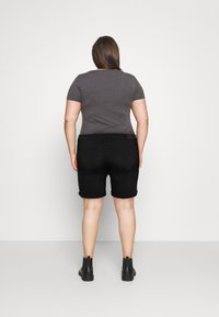 Šedé tričko s krátkým rukávem spárované s černými džínovými šortkami s ohrnutým lemem. Nošeno s černými kotníkovými botami, pohled zezadu.