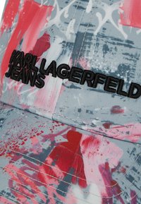 Gorra con un patrón de salpicaduras multicolor en rojo y rosa sobre un fondo gris, con "KARL LAGERFELD JEANS" bordado en negro.