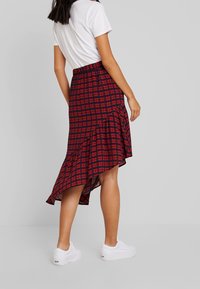 Rood en marineblauw geruite midi-rok met een asymmetrische zoom, elastische tailleband en ruffles; gedragen met een wit T-shirt en witte sneakers.