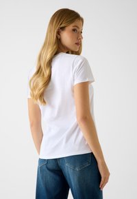 Weißes Baumwoll-T-Shirt mit kurzen Ärmeln, rundem Halsausschnitt und lockerem Schnitt, kombiniert mit dunkelblauen Jeans mit Gesäßtaschen.