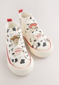 Baskets montantes blanches avec des taches noires de vache, une bordure rouge et des décorations de personnages de dessin animé Woody et Jessie sur les lacets.