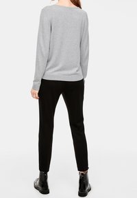 Grijze lange mouwen trui met een ronde hals, gecombineerd met zwarte tapered broek en glanzende zwarte enkellaarsjes, bekeken vanaf de achterkant.