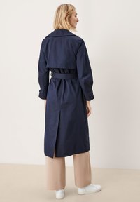 Laivan sininen trench-coat, jossa on vyöllinen vyötärö, ylisuuressa kauluksessa ja selkäventtiili. Malli yhdisti sen beigeisiin leveälahkeisiin housuihin ja valkoisiin lenkkareihin.