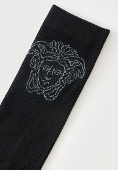 Chaussette noire côtelée avec un motif tête de Méduse bleu clair tricoté près de la bordure supérieure.