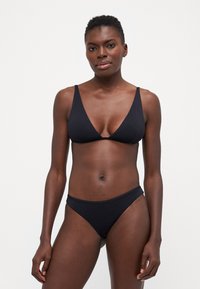 Juodasis bikini rinkinys su trikampiu viršumi su plonomis petnešėlėmis ir atitinkančiais žemais liemeniu apatiniais, pagamintas iš lygios, elastingos medžiagos.