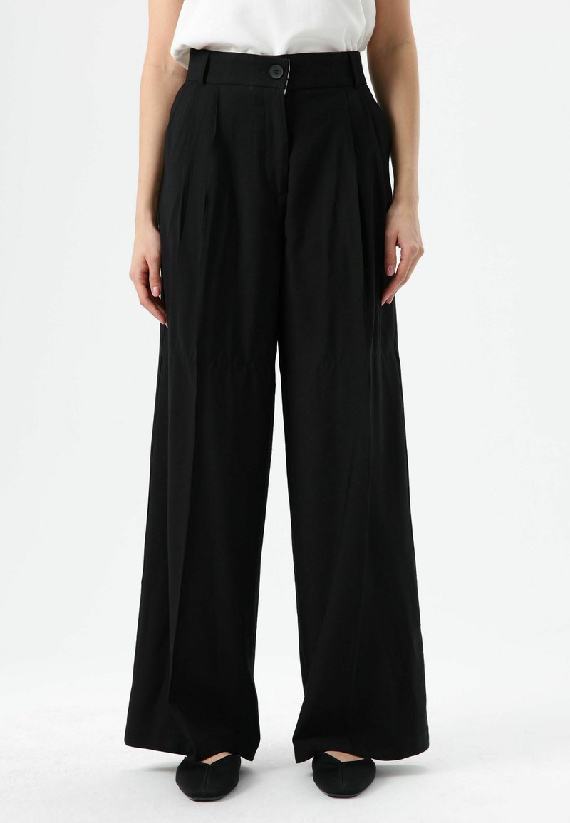 Schwarze, weit geschnittene Hosen aus glattem Stoff mit hoher Taille, Bügelfalten und Knopfverschluss vorne. Weiche Textur und maßgeschneiderte Passform.