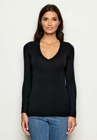 Schwarzes langärmliges Oberteil mit V-Ausschnitt, glatter Textur, figurbetontem Design und gerafften Details an den Ärmeln, kombiniert mit blauen Jeans.