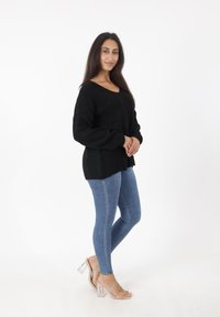 Czarny dzianinowy sweter z dekoltem w serek, połączony z dopasowanymi niebieskimi dżinsami i przezroczystymi sandałami na słupku. Prosty i teksturowany fason.