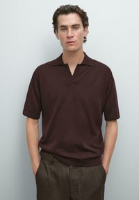 Brun kortärmad polo med öppen krage, slät textur, kombinerad med mörka byxor, mot en neutral bakgrund.