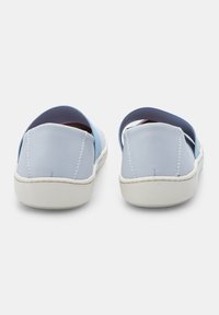 Ljust blåa skosläp med ovandel i mjukt läder, elastisk rem och vit gummisula; slät yta med synliga sömnadsdetaljer.