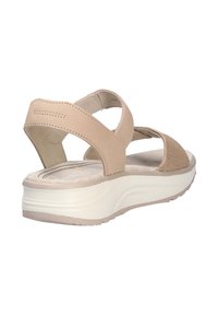Sandal de color beige con tiras cruzadas y un acento texturizado. Suela blanca gruesa con un patrón ondulado, plantilla plana y material de cuero suave.