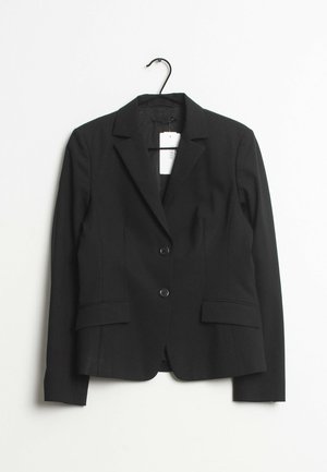 Blazer noir ajusté avec revers crantés, deux boutons, poches à rabat et manches longues suspendu à un cintre noir sur un fond blanc.