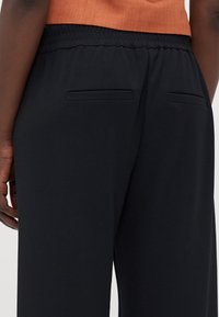 Zwarte stretchbroeken met een comfortabele elastische tailleband, twee verborgen achterzakken en een gladde textuur.