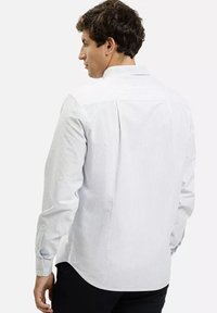 Biała koszula z długim rękawem zapinana na guziki, z cienkimi pionowymi paskami i prostym karczkiem z tyłu, wykonana z gładkiego bawełnianego materiału.