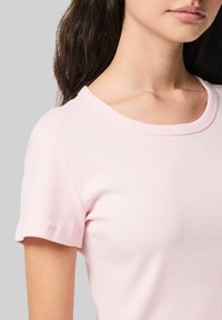 Gaiši rozā ribotā īsām piedurknēm T-kreklu ar apaļu kakla izgriezumu un pieguļošu siluetu, kas izceļ gludu tekstūru.