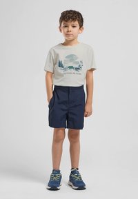 Ανοιχτό γκρι μπλουζάκι με μπλε γραφικό αρκούδας και δέντρων, σε συνδυασμό με σκούρα μπλε σορτς. Το αγόρι φοράει μπλε αθλητικά παπούτσια με πράσινες λεπτομέρειες.