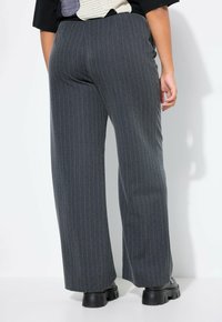 Kalhoty širokého střihu v tmavě šedé látce s proužkovaným vzorem. Mají vysoký pas a strukturovaný povrch, doplněné o masivní černou obuv.