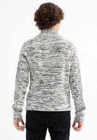 Jersey de punto en tonos gris y blanco apagado, con cuello alto, patrón texturizado y mangas ajustadas, combinado con pantalones negros.