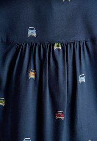 Navy fabric dress with small, multicolored vintage car patterns. Features gathered texture at the waist, creating a flowing appearance.