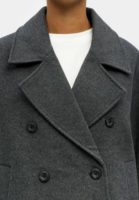 Manteau double boutonnage en mélange de laine gris, avec de grands revers, des boutons noirs, un tissu texturé et une coupe ajustée.