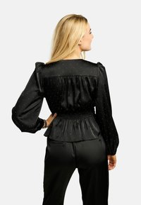 Czarna satynowa bluzka z bufkami i marszczonym paskiem w talii. Posiada białe kropki, miękką teksturę i swobodny fason.